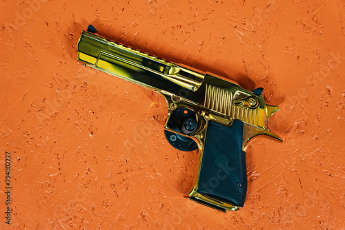 Big gold pistol gainst an orange wall. photo