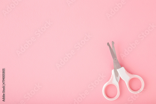 Scissors for baby nail cutting on light pink table background. Pastel color. Closeup. Empty place for text. Top down view.