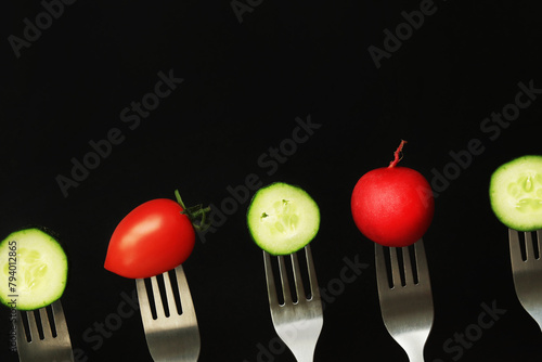 Tomato, cucumber and radish on forks, close-up, dark background. Healthy eating concept. Fresh vegetables in the diet. Vegetables on a black background. Space for text