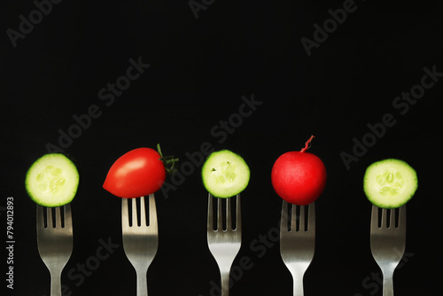 Tomato, cucumber and radish on forks, close-up, dark background. Healthy eating concept. Fresh vegetables in the diet. Vegetables on a black background. Space for text