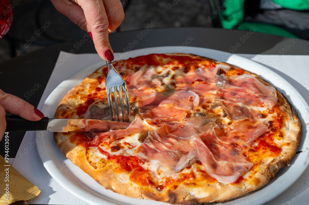 Eating of fresh baked pizza dish in italian pizzeria restaurant, Prosciutto di Parma