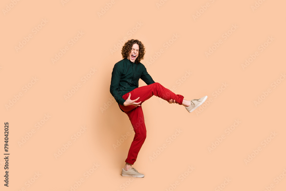 Photo portrait of handsome young guy dancing have fun play leg guitar dressed stylish green garment isolated on beige color background