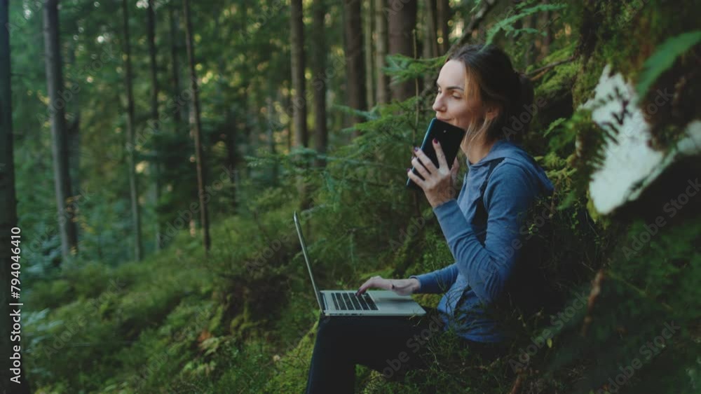 Woman work on laptop and talking mobile phone sitting near moss stone in sunset forest. Tourist girl typing on notebook, rest stop in hiking route. Outdoor lifestyle travel summer holiday vacation. Woman work on laptop and talking mobile phone sitting near moss stone in sunset forest. Tourist girl typing on notebook, rest stop in hiking route. Outdoor lifestyle travel summer holiday vacation.