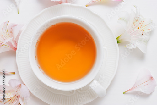 Cup of healthy organic tea close up with flowers at the background, top view.
