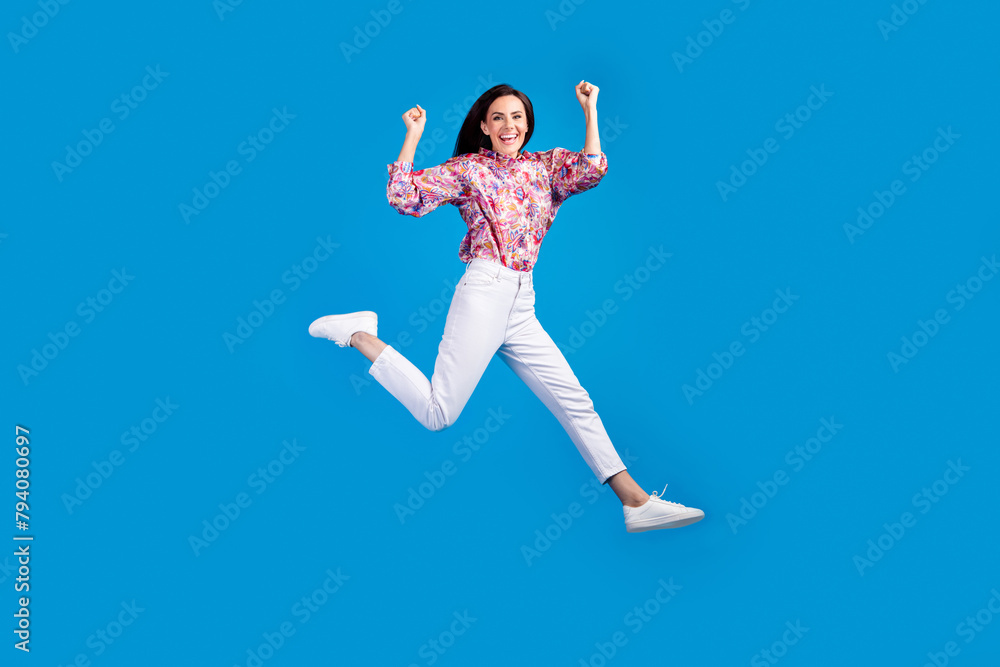 Full length photo of lucky funky lady dressed print blouse jumping high having fun isolated blue color background