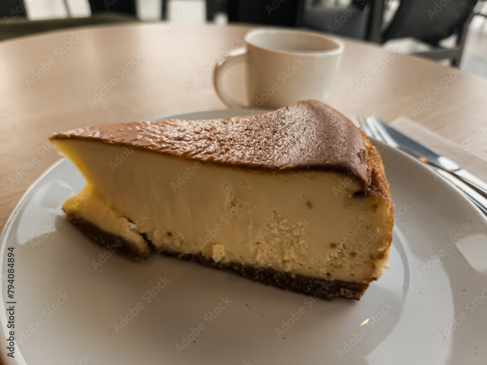 Obraz premium A slice of San Sebastian Cheesecake on a plate with a coffee in a cafe 