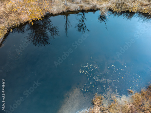Aerial look down on river blue water surface with reeds on autumn riverbanks