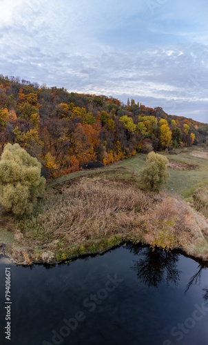 Aerial calm river shore in colorful autumn valley with cloudy sky in Ukraine