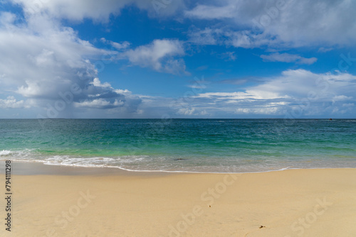 La vue s'étend sur la mer bleue, où le ciel et les nuages se rencontrent à l'horizon, tandis que le sable et les eaux turquoises de la Bretagne sont ornés d'une écume blanche.