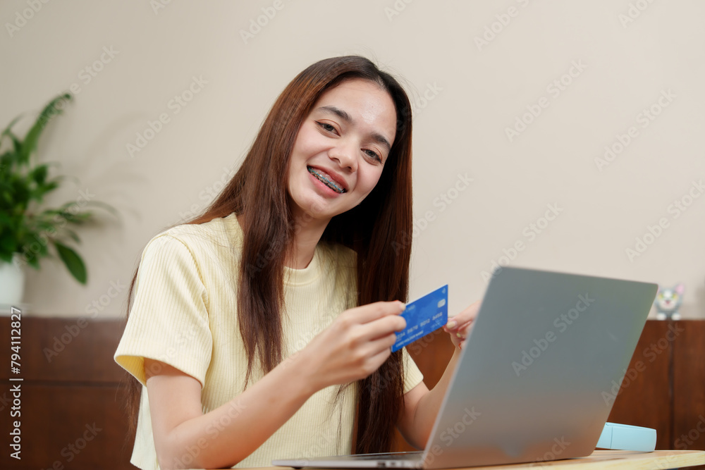 Radiant asian lady with braces presents credit card, engaging in e-commerce with a portable computer at home. Delighted consumer . Radiant asian lady with braces presents credit card, engaging in e-commerce with a portable computer at home. Delighted consumer .