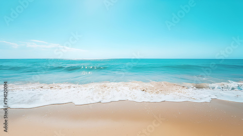 Beach scene with clear turquoise waters gently lapping onto the sunlit sandy shore under a bright blue sky.