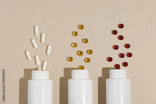 Three white mockup jars with white, yellow and red pill capsules on beige isolated background. Concept of pharmacy, health, dietary supplements and medical products. Image for your design