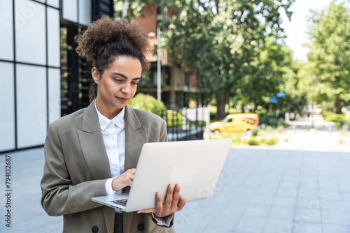Portrait of young successful businesswoman office worker using laptop computer outside office building in formal wear. Professional female business person working outdoor online, checking information