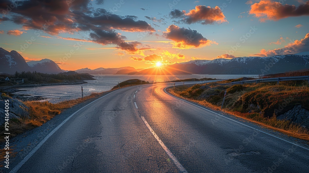 A road with a sunset in the background. The road is wet and the sun is setting. The sky is cloudy and the sun is shining through the clouds