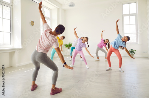 Dance fitness class. Active group of preteen kids practice hip-hop with female trainer during dance class. Girl group of little dancers learning modern dance movements in bright, spacious hall.
