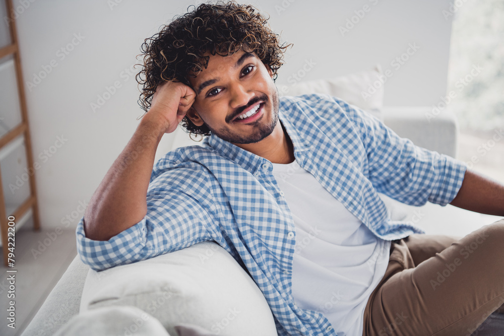 Photo of handsome cheerful guy dressed plaid shirt enjoying weekend sitting sofa indoors room home house Photo of handsome cheerful guy dressed plaid shirt enjoying weekend sitting sofa indoors room home house