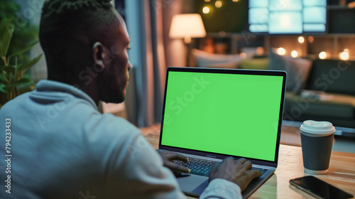 Laptop is used by a man looking at a green screen. Freelancer is seen working remotely from home. He is typing on the keyboard, and browsing internet close up photo