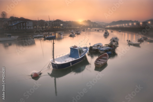 Boats at dawn in the Plentzia estuary with the sun rising behind the mountains leaving a warm atmosphere and an orange sky