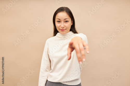 Pretty smiling asian girl in sweater standing against pink studio background, pointing at camera with finger out of focus, choosing you, motivating to move on, go ahead, achieve your goals