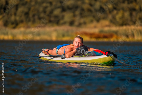 relaxed woman resting on a SUP paddleboard on a sunny day in a calm river