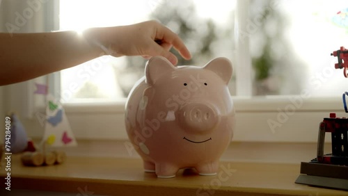 Child throwing money into piggy bank on desk and saving money in front of window