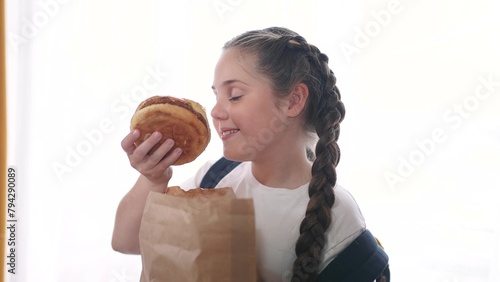 schoolgirl child eating hamburger breakfast at recess. training nutrition for schoolchildren fast food concept. schoolgirl child eating breakfast sandwich from a paper lifestyle bag with a backpack