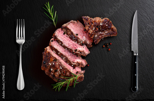 Rib eye beef sliced on black flavored stone with fork knife