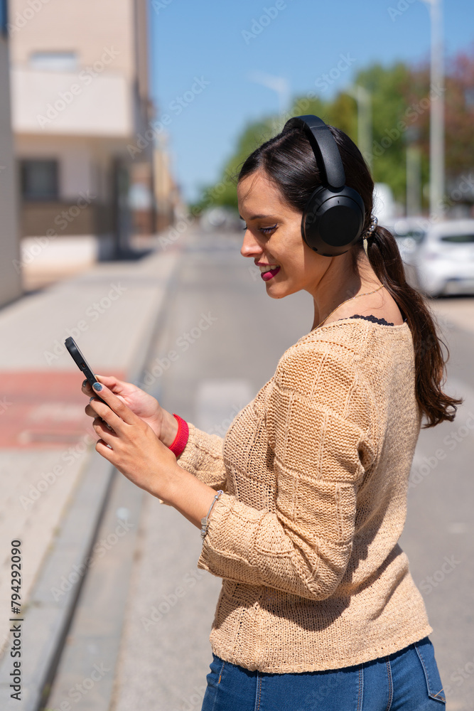 Fototapeta premium Beautiful woman listening to music with headphones and her cell phone in the street