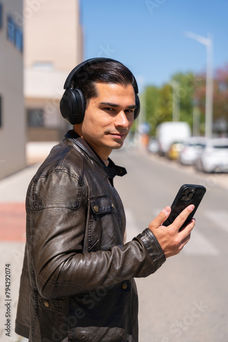 Modern and handsome man listening to music with headphones and his cell phone on the street.