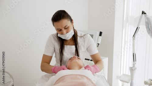 The cosmetologist applies chemical peeling. Close-up of beautician using cosmetic brush while applying facial jelly gel to female client's face in beauty clinic.