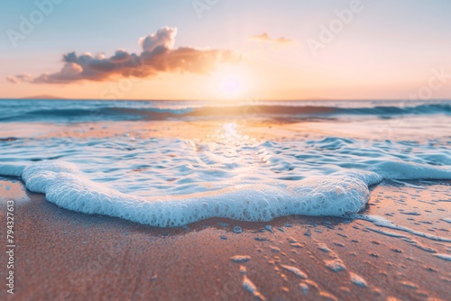 Golden sunrise over the ocean with gentle waves and frothy surf on sandy beach.