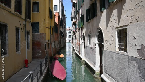 Venetian old narrow canals with buildings on both sides and boats parked on water.