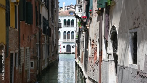 Venetian old narrow canals with buildings on both sides and boats parked on water.