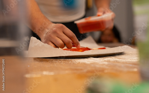 Chef Preparing Pizza Base with Fresh Tomato Dish in Restaurant Kitchen, Blurry Background
