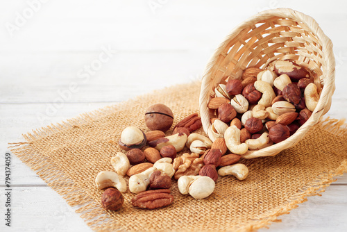 Nuts Mix in a Wooden Plate on a White Background. Wicker Basket full of Cashew, Walnuts, Hazeltuts, Peanuts, Brazilian Nuts, Pistachios on a Burlap with Side View