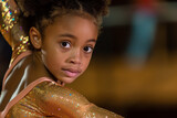 A young girl gymnast in a sparkly leotard is looking over her shoulder at the camera.