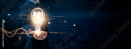 API: Businessman Holding Creative Light Bulb with Digital Networking and API Icon. Innovation, Integration, Connectivity, on Blue City Background. photo