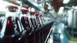 A row of bottles of soda are on a conveyor belt. The bottles are red and clear