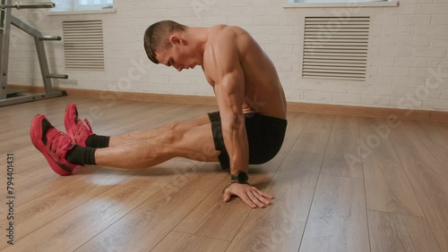 Bodybuilder in black shorts training in gym and performs swings bent legs in table pose. This exercise works abdominal and leg muscles and strengthens triceps photo