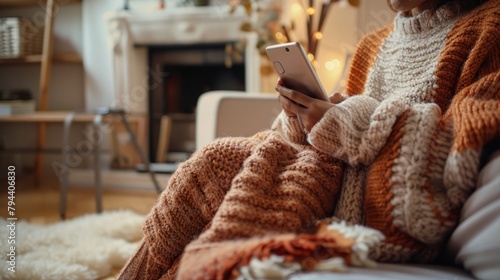 Cozy winter scene with hands holding a smartphone, soft knitwear, comfort at home.