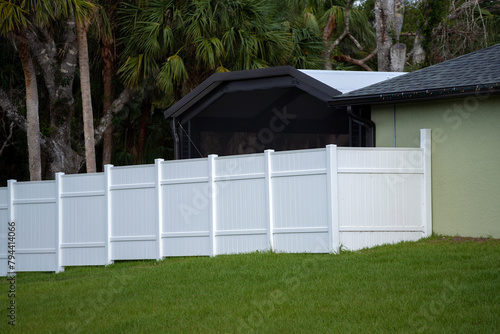 White vinyl picket fence on green lawn surrounding property grounds for backyard protection and privacy