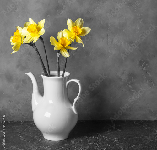 bouquet of yellow daffodil flowers in a light vase on a dark background