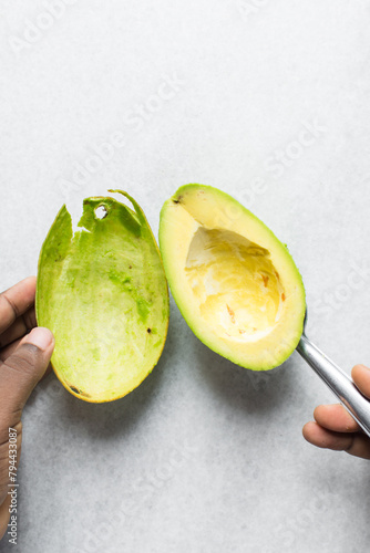 Overhead view of green avocado being peeled using a spoon, top view of avocado being de-skinned with a silver spoon