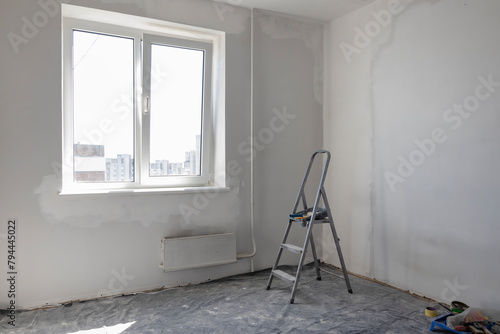 A metal ladder in the room. An empty room during renovation. The concept of repair in the house.