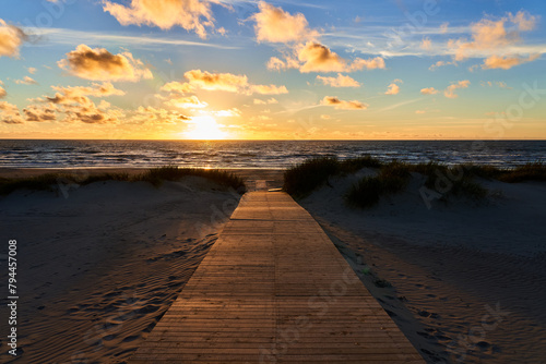A wooden road leads to the ocean during sunset. A landscape stretching into the distance