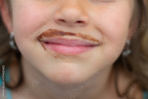 Detail of a white girl's mouth with a dirty chocotale mustache after drinking a glass of milk with chocolate. Child nutrition.