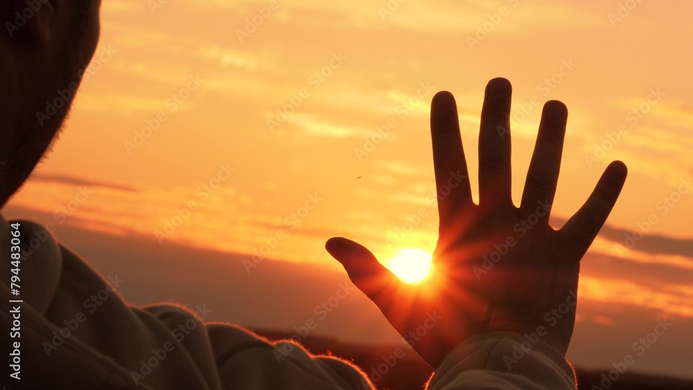 Silhouette of hand at orange sunset. Man stretches hand towards sun, warming palm in summer rays. Unity with nature, enjoyment of trip. Guy gains strength, contemplating, enjoying solitude with nature