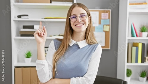 Cheerful, young blonde business worker, elatedly pointing to both sides with her hands in the office, smiling broadly at the camera while presenting her brilliant ideas photo