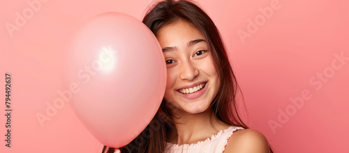 Young smiling woman holding a balloon and looking at it on a pink background. Banner template for holiday agency.