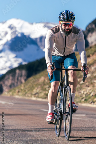 A man cycling down a straight road with a large snow-capped mountain in the background.